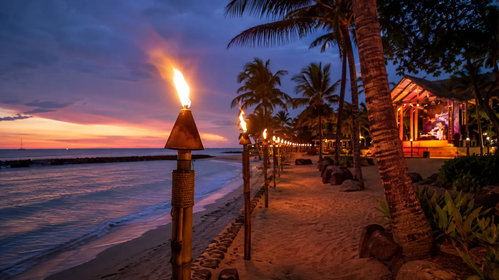 Tiki-Fackeln entlang eines palmengesäumten Strandes auf Oahu bei Dämmerung