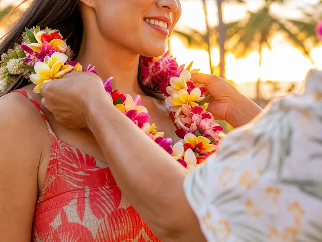 Frische Leis aus Plumeria und Orchideen werden einem Gast bei Sonnenuntergang umgelegt